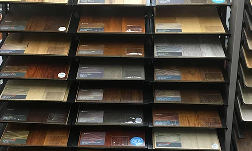 Wall of shelves displaying various types of wood flooring samples in a J&S Hardwood Flooring store