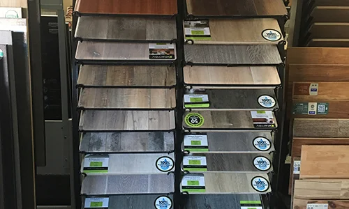 Assortment of wooden flooring samples displayed in various colors and patterns, each labeled with a brand logo.