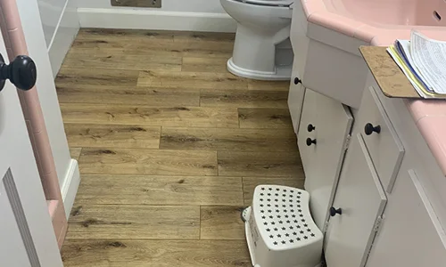 A white toilet sitting next to a pink sink in a bathroom hardwood flooring